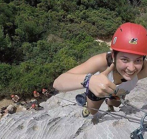 Eine Schülerin aus der Kletter AG klettert an einer Felswand hoch und zeigt mit dem Daumen nach oben.