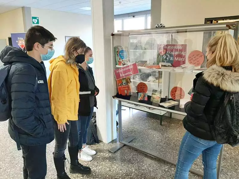 Schülerinnen und ein Schüler stehen vor dem Schaukasten der Schulbibliothek.